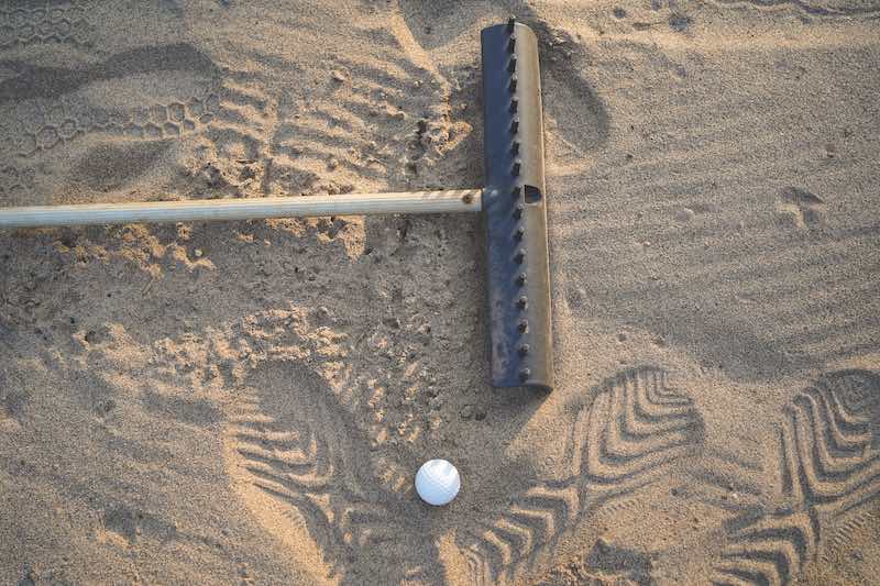 Golf concept. Golf ball and rake sand on bunker in beautiful golf course at sunset background.